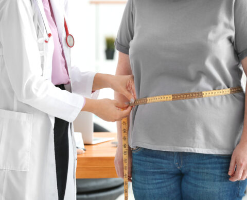 Young female doctor measuring waist of overweight woman with centimeter in clinic