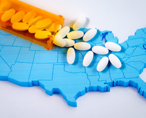 White pharmaceutical pills spilling from prescription bottle over American flag