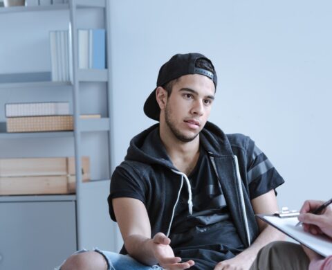 A rebel teenage boy with behavioral problems and criminal past talking to a psychotherapist in a juvenile detention center.